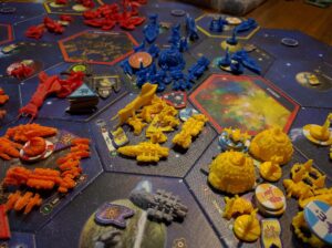 A close-up view of a colorful and detailed board game layout featuring various brightly colored plastic pieces representing spaceships and starbases, arranged on a galaxy-themed game board with hexagonal spaces, alongside cards and tokens.