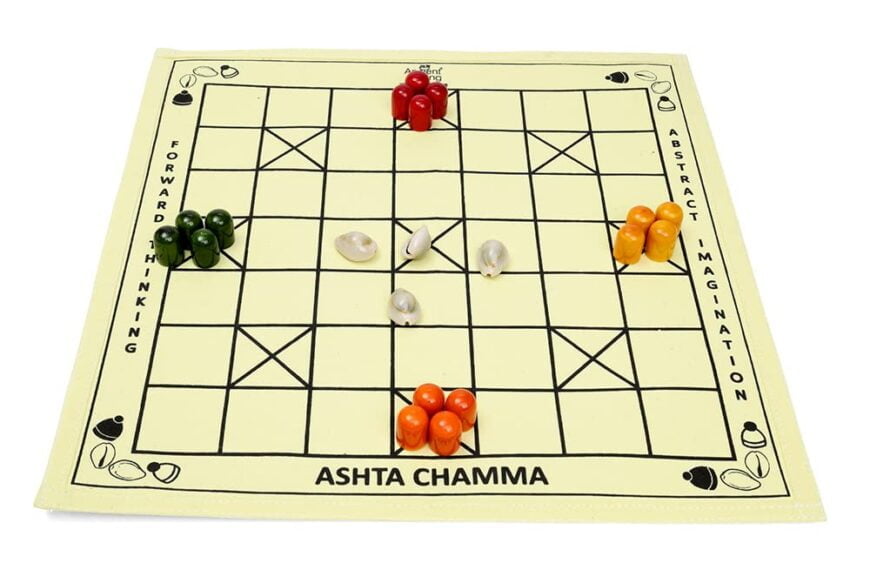 A traditional Ashta Chamma board game setup with four groups of colored tokens: red, orange, green, and white shells, arranged at the starting points on the board.