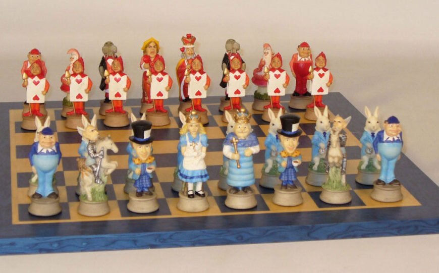 A themed chess set featuring characters from 'Alice in Wonderland' with pieces shaped like the White Rabbit, Alice, the Mad Hatter, and others, arranged on a chessboard.