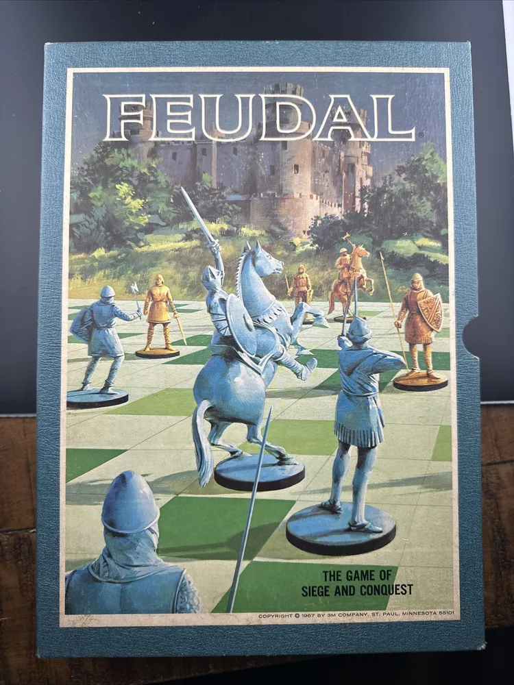 A board game titled "FEUDAL: THE GAME OF SIEGE AND CONQUEST" with illustrated medieval figures such as knights and archers on a chessboard-like grid with a castle background, indicating a strategy game. The bottom of the image indicates a copyright of 1967 by 3M Company, St. Paul, Minnesota.