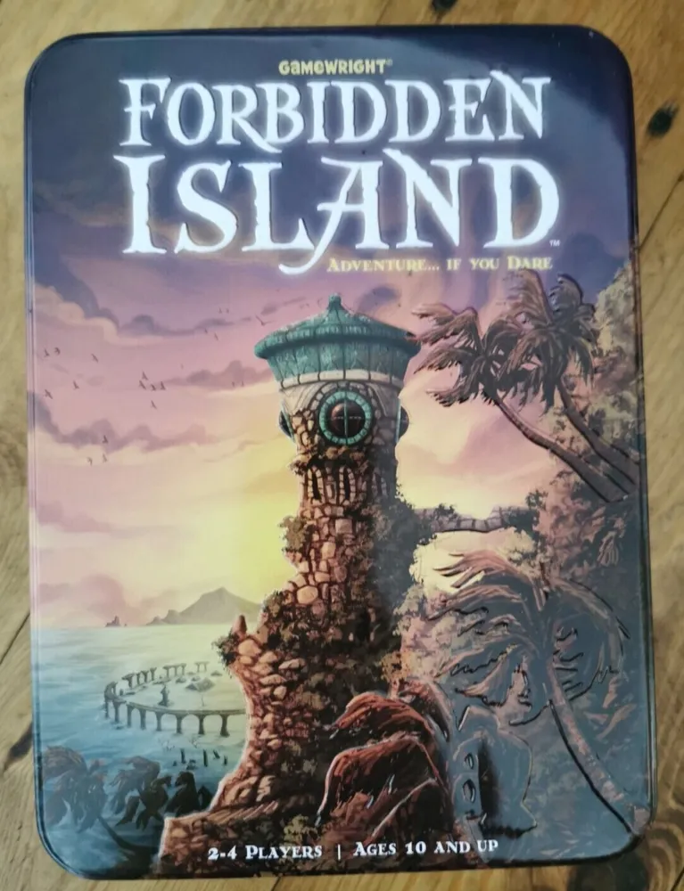 A board game box titled "Forbidden Island" by Gamewright, with an artistic depiction of a lighthouse on a cliff, palm trees, and a sunset sky. Text on the box indicates it's for 2-4 players, ages 10 and up.