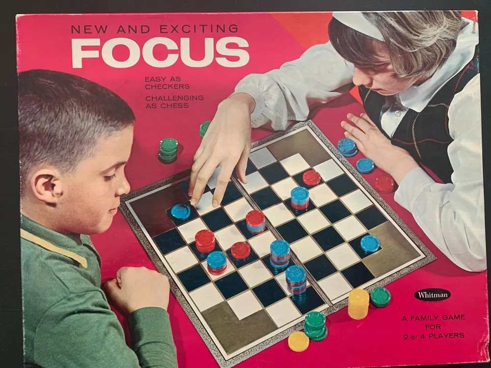 Two children are playing a strategic board game called Focus, with one child reaching out to move a piece. The game is described as "Easy as Checkers, Challenging as Chess." The box art includes the game's title and notes that it is suitable for 2 or 4 players.