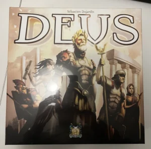A board game cover featuring illustrated ancient Roman or Greek themed characters, including a central figure holding a trident and wearing a laurel wreath, with the title "DEUS" in large letters above. The cover also displays the name Sébastien Dujardin and the Pearl Games logo at the bottom.