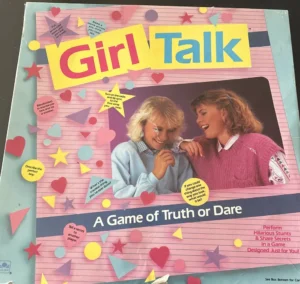 Vintage "Girl Talk" board game box cover featuring two smiling young women with 80s hairstyles, wearing sweaters. The cover is decorated with colorful stars, hearts, and speech bubbles containing text, highlighting the game's truth or dare concept.