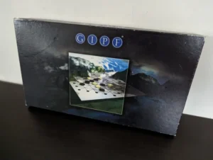 A worn board game box for "GIPF" standing on a table with a visible cover featuring an abstract design and a picture of the game pieces on a hexagonal board.