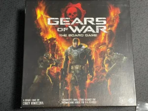A board game titled "Gears of War: The Board Game" with an illustration of armed characters in combat gear on the cover, featuring a fiery background with a large skull emblem. The bottom text attributes the game to Corey Konieczka and indicates it is for 1-4 players.