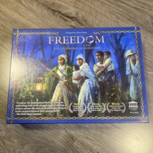 A board game box titled "FREEDOM: THE UNDERGROUND RAILROAD" on a wooden surface, with an illustration of people dressed in 19th-century clothing trekking through a forest. The box also displays awards and accolades, and the text, "Designed by Brian Mayer."