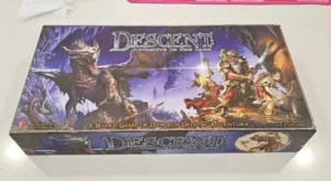 A "Descent: Journeys in the Dark" board game box displaying fantasy artwork with a dragon and heroes on a table.