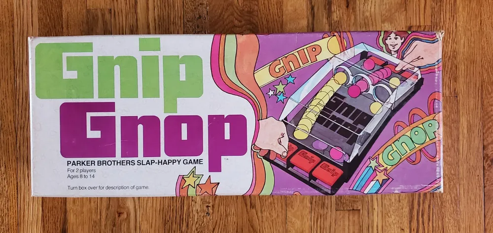 Vintage "Gnip Gnop" game box by Parker Brothers, indicating it's for 2 players aged 8 to 14, with a colorful illustration of the slap-happy game on a wooden background.