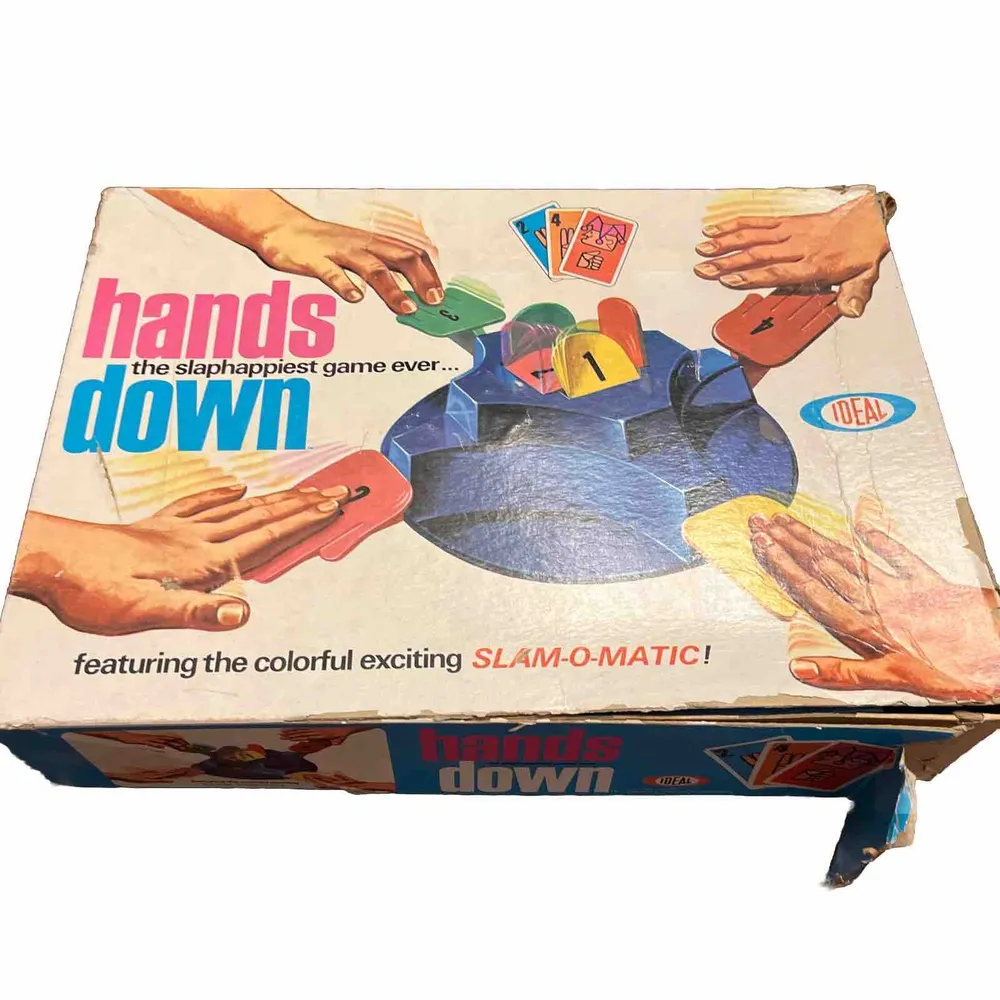 Vintage "Hands Down" board game box with an image showing hands slamming down on a colorful game unit with cards, labeled as "the slaphappiest game ever... featuring the colorful exciting SLAM-O-MATIC!" by IDEAL.