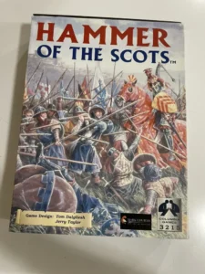A board game cover titled "HAMMER OF THE SCOTS" with a dynamic illustration of medieval soldiers in battle. The game design is credited to Tom Dalgliesh and Jerry Taylor, with a logo for Columbia Games and a reference number 3215 on the bottom right.