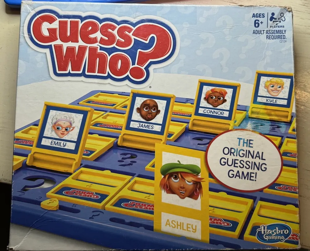 Box cover of "Guess Who?" board game by Hasbro Gaming, featuring cartoon character portraits with names like Emily, James, Connor, and Kyle, and a tagline stating "THE ORIGINAL GUESSING GAME." The game is for ages 6+ and requires adult assembly.
