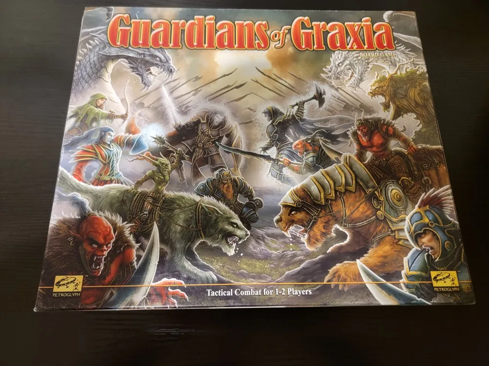 A board game box for "Guardians of Graxia," featuring vibrant fantasy artwork with various characters and creatures engaged in battle, labeled as Tactical Combat for 1-2 Players.