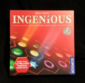 The image shows the board game "Ingenious" by Reiner Knizia, labeled as the ultimate family strategy game, with a tag noting "more than 1.3 million ingenious games sold." The game's box, with a red background featuring abstract colorful shapes, is published by Kosmos.