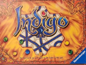 Box cover for the board game "Indigo" by Reiner Knizia, featuring stylized title text with jewel-toned colors and decorative elements, and multiple languages indicating "The Game" along with the Ravensburger logo.
