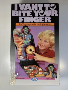 Box cover of "I VANT TO BITE YOUR FINGER" board game depicting a cartoon vampire, a smiling young boy pointing at a clock, and images of the game components with text indicating it's for 2 to 4 players ages 5 and up.