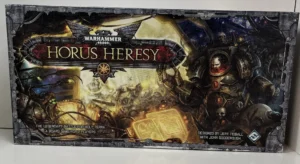 Boxed board game "Warhammer 40,000: Horus Heresy" displaying artwork of armored figures and futuristic battlefield imagery, with text indicating it is designed by Jeff Tidball with John Goodenough for 2 players.