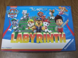 A "Paw Patrol Junior Labyrinth" board game box featuring cartoon images of the Paw Patrol characters and a maze on the cover, designed for ages 4 and up. The box is adorned with the Nickelodeon logo and indicates Max J. Kobbert as the creator, with the Ravensburger brand at the bottom.