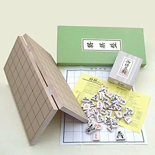 A Shogi (Japanese chess) game set with the board partially unfolded, pieces spilled onto the board, and some instructional papers, all next to its open green box with Japanese characters.
