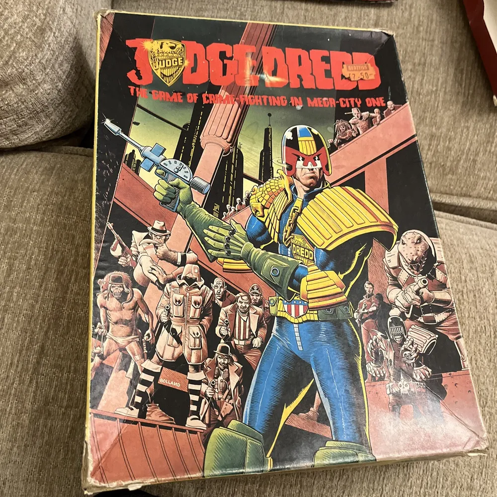 Worn-out "Judge Dredd" board game box with an illustration of the character Judge Dredd holding a gun, surrounded by other futuristic characters and a cityscape in the background.