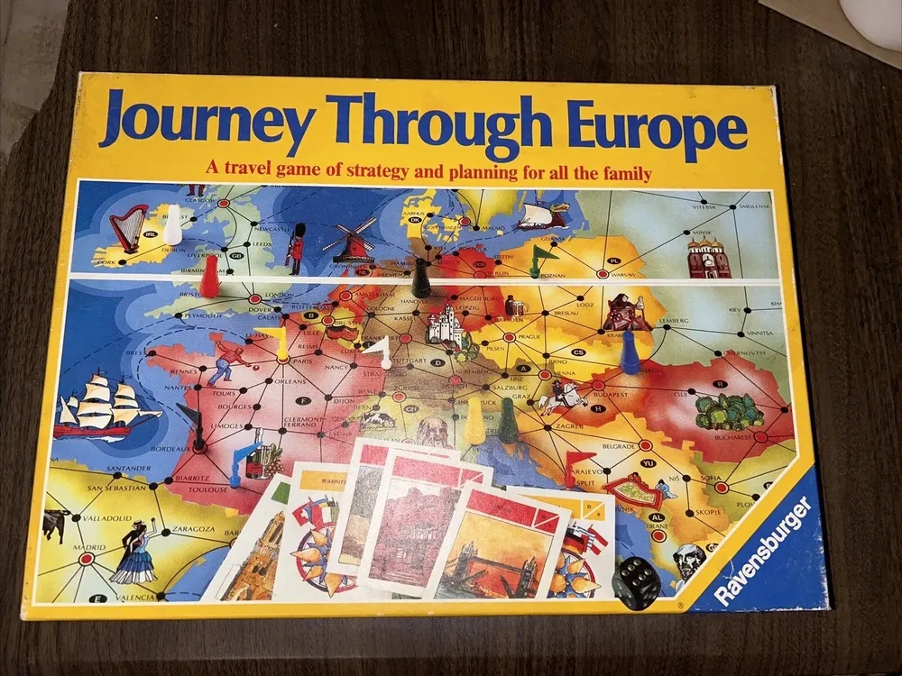 Board game "Journey Through Europe" displayed on a table, including a colorful map of Europe, game pieces, cards, and dice, with the logo "Ravensburger" on the bottom right corner.