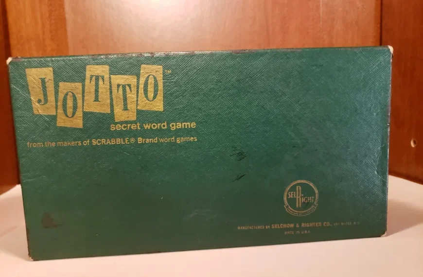 A vintage "JOTTO secret word game" box with worn green cover, gold lettering, and the SCRABBLE brand logo, manufactured by Selchow & Righter Co., displayed against a wooden backdrop.