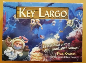 Board game cover for "Key Largo" featuring cartoon divers exploring an underwater scene with sunken treasures, colorful marine life, and a prominent diver in the foreground. Text on the cover reads, "A family board game of sun, sand, and salvage!" by Paul Randles, with Mike Selinker and Bruno Faidutti.