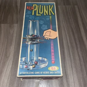 Vintage "KerPlunk" board game box by Ideal featuring a clear plastic tower filled with colorful balls supported by sticks, with hand pulling one stick, and illustrations of excited faces in the background. The box reads "A TANTALIZING GAME OF NERVE AND SKILL."