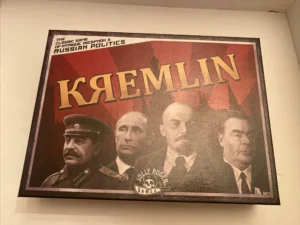 A board game titled "KREMLIN" bearing the subtitle "The Classic Game of Intrigue & Russian Politics", with illustrations of four figures on the cover art, displayed against a red and brown background with the logo of "Jolly Roger Games" on the bottom right corner.