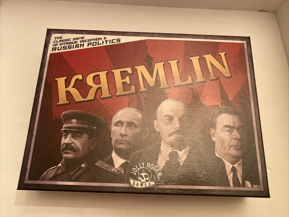 A board game titled "KREMLIN" bearing the subtitle "The Classic Game of Intrigue & Russian Politics", with illustrations of four figures on the cover art, displayed against a red and brown background with the logo of "Jolly Roger Games" on the bottom right corner.