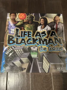 Board game cover titled "Life as a Blackman the Game" featuring illustrations of diverse characters, including a basketball player, soldier, and businessperson, against an urban backdrop with buildings and a stylized title design.