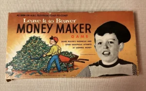 Vintage 'Leave it to Beaver Money Maker Game' board game box, featuring a drawn character pushing a wheelbarrow full of money next to a large photo of a boy's head, with text mentioning the TV show and the game's premise of earning money. The box shows wear and tear around its edges.