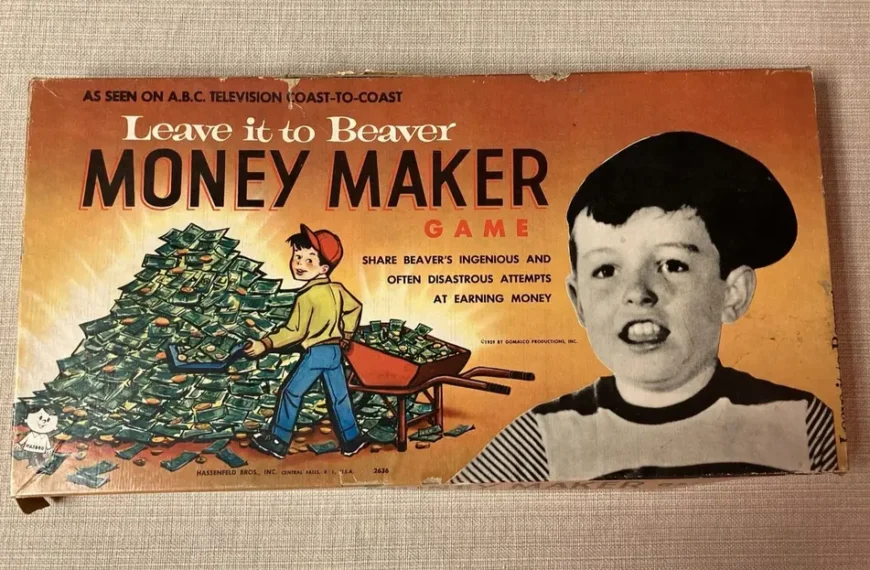 Vintage 'Leave it to Beaver Money Maker Game' board game box, featuring a drawn character pushing a wheelbarrow full of money next to a large photo of a boy's head, with text mentioning the TV show and the game's premise of earning money. The box shows wear and tear around its edges.
