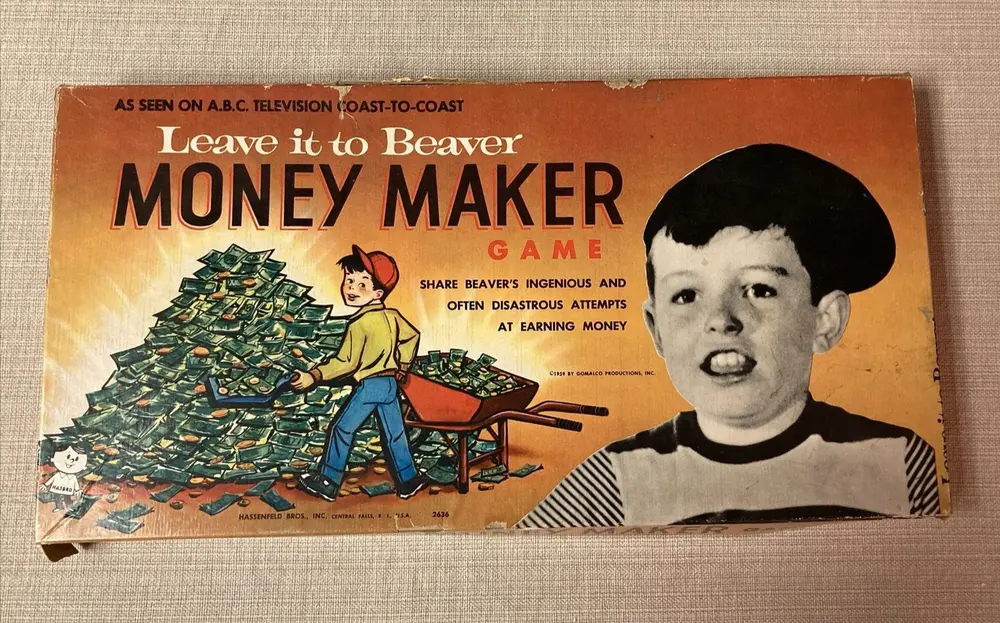 Vintage 'Leave it to Beaver Money Maker Game' board game box, featuring a drawn character pushing a wheelbarrow full of money next to a large photo of a boy's head, with text mentioning the TV show and the game's premise of earning money. The box shows wear and tear around its edges.