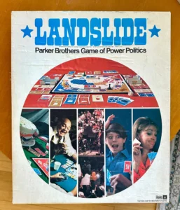 Box cover of "LANDSLIDE Parker Brothers Game of Power Politics," featuring a circular window with images of a crowded rally, a man shaking hands, a child on a phone, and a woman with a clipboard, overlaying a game board background.