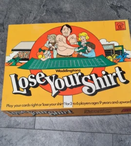 Board game "Lose Your Shirt" by Waddingtons on a tile floor, featuring cartoon illustrations of people around a table, with a horse race in the background, and text "Play your cards right or 'lose your shirt!' for 3 to 6 players ages 9 years and upwards".
