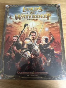 A "Lords of Waterdeep" board game box featuring illustrated fantasy characters prepared for battle, with the Dungeons & Dragons logo at the bottom, indicating that the game is for 2 to 5 players and suitable for ages 12 and up.