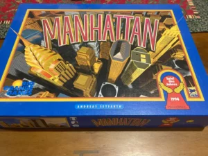 A board game titled "MANHATTAN" by Rio Grande Games, designed by Andreas Seyfarth, with an illustration of stylized skyscrapers on the cover. The box also features a "Spiel des Jahres 1994" (Game of the Year 1994) award badge.