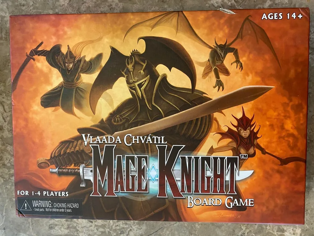 Box cover of Mage Knight Board Game depicting fantasy characters including mages and dragons with game title and designer's name, Vlaada Chvátil, suitable for ages 14 and up, warning for choking hazard due to small parts.