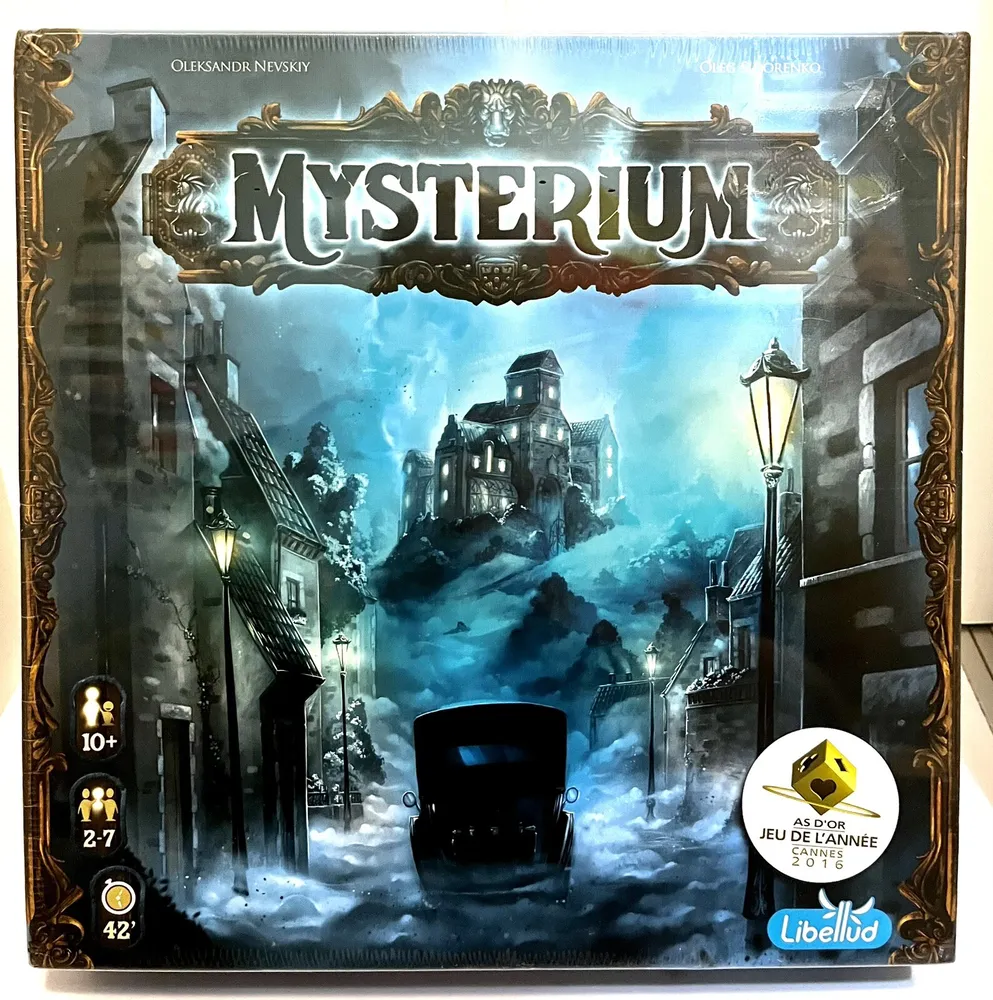 Box cover of the board game "Mysterium" depicting a gloomy, snowy street scene with a vintage car, street lamps, and a mysterious mansion in the background, designed by Oleksandr Nevskiy and Oleg Sidorenko, indicating age 10+, for 2-7 players, with a typical game length of 42 minutes, and a recipient of the "As d'Or Jeu de l'Année 2016" award, by publisher Libellud.