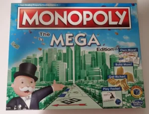 A Monopoly Mega Edition board game box featuring the Monopoly man in front of a cityscape, with money and property cards flying around, and taglines stating "Own More!", "Build More!", "Get Richer!", and "Play Faster!".