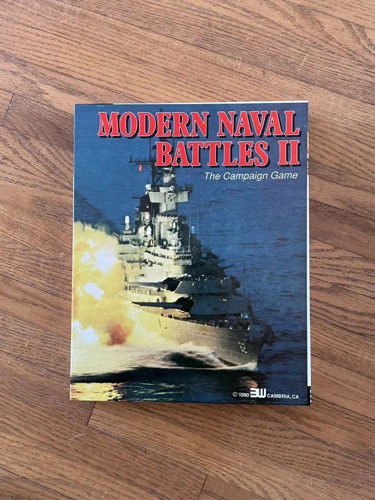 Board game titled "MODERN NAVAL BATTLES II The Campaign Game" with an image of a battleship on the cover, placed on a wooden floor.