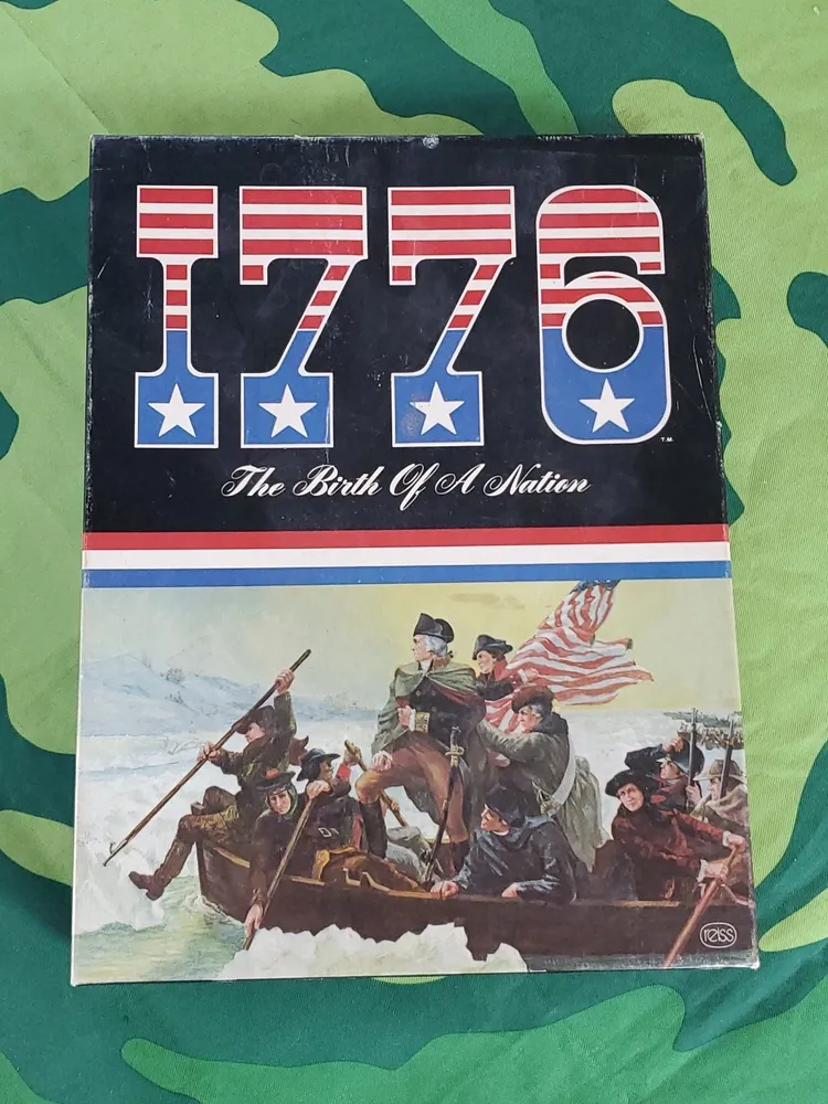 Board game titled "1776 The Birth Of A Nation," depicting Revolutionary War soldiers in a boat with the American flag, resting on a green camouflage background.