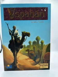 Alt text: The boxed board game "Yspahan" by Sebastien Pauchon, with cover art depicting a man riding a camel in a desert setting with a city and its domed buildings in the background. The logos of Rio Grande Games and Ystari Games are visible on the cover.