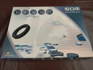 A photo of the board game "YINSH" by Kris Burm, displaying the game's box which features the game's title, the author's name, various playing pieces, and labels indicating it is a pure strategy game from the GIPF project series.