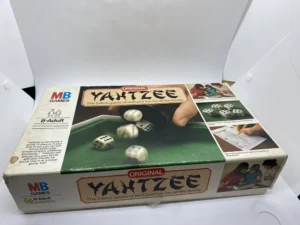 An "MB Games" original Yahtzee board game box for ages 8 to adult, displaying the game's title, dice images, and people playing the game, on a white background.