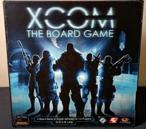 Box cover of "XCOM: The Board Game," featuring silhouetted figures in combat gear against a futuristic backdrop with the Earth and game's logo illuminated above. Text on box reads "A Board Game of Global Defense for 1-4 Players by Eric M. Lang" along with publisher logos.
