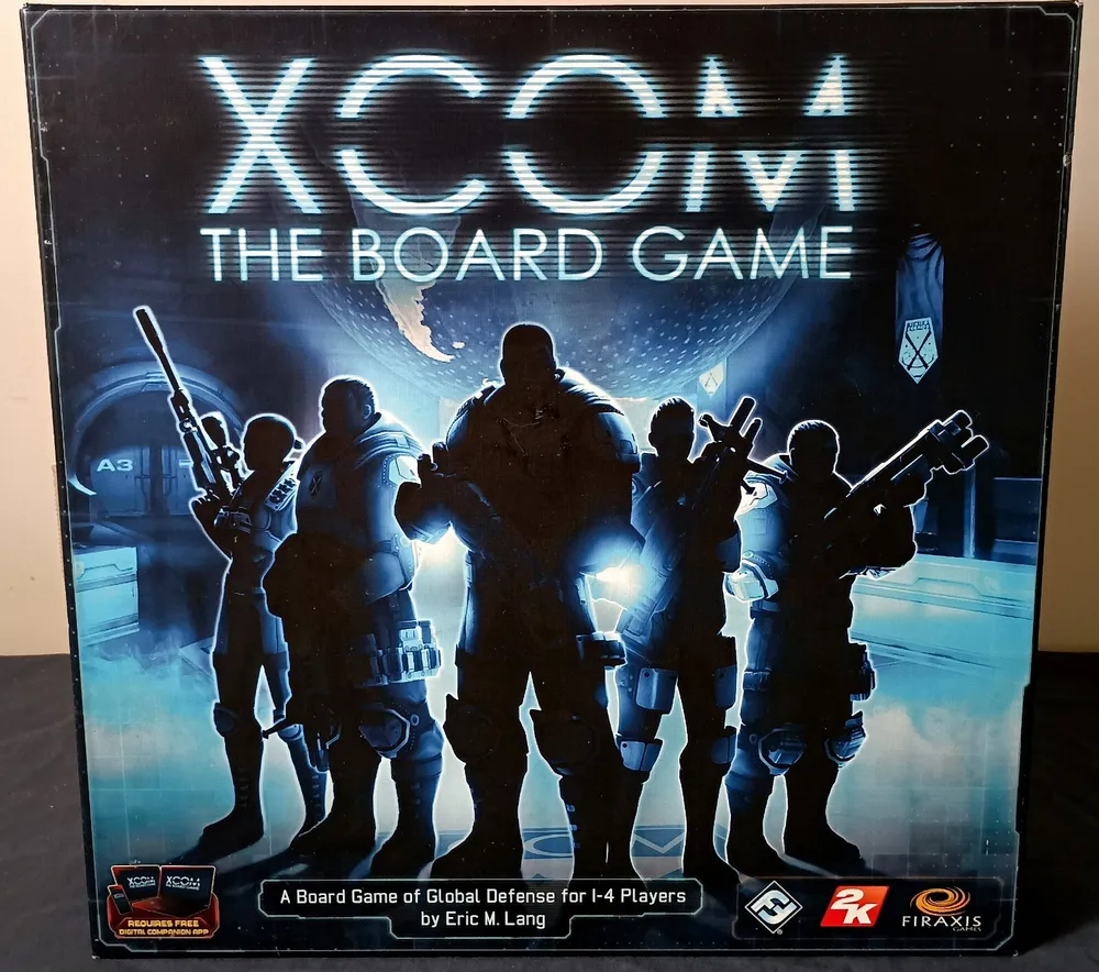 Box cover of "XCOM: The Board Game," featuring silhouetted figures in combat gear against a futuristic backdrop with the Earth and game's logo illuminated above. Text on box reads "A Board Game of Global Defense for 1-4 Players by Eric M. Lang" along with publisher logos.