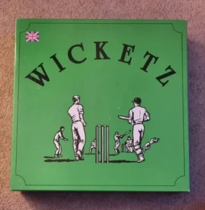 A green book cover with the title "WICKETZ" in large black letters at the top and a stylized illustration of cricket players in white attire in various action poses around the cricket stumps, with a small Union Jack flag in the top left corner.