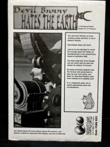 An advertisement for a board game titled "Devil Bunny Hates the Earth," described as a Cheapass Board Game for 2-5 players. The text outlines the premise of the game where players are candy machines in Devil Bunny's factory trying to thwart his plan to destroy the earth with unsatisfying saltwater taffy. The requirements for the game, including pawns, counters, and a six-sided die, are listed at the bottom, alongside a black-and-white drawing of a squirrel and a pair of pawns. The Cheapass Games logo and item number are also visible.